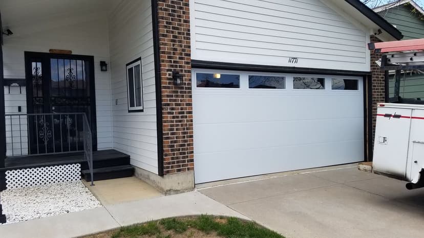 Modern house exterior featuring a white garage door, brick facade, and porch steps.