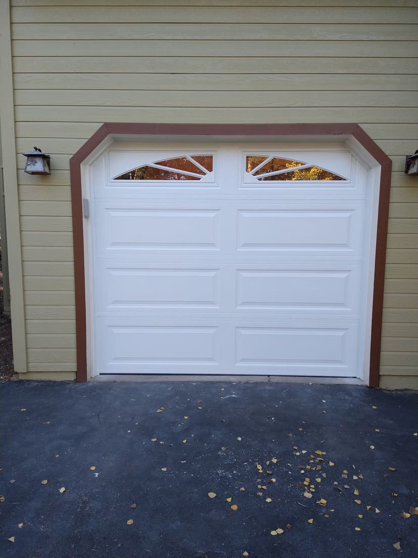 White garage door with decorative windows, framed by brown accents against a yellow house.